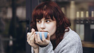 Junge Frau trinkt aus einer Tasse: Sind Tee und Kaffee Kalziumräuber und schlecht für die Knochen?