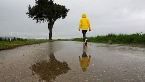 Eine Frau mit Regenjacke geht alleine auf einem Feldweg spazieren: Immer mehr junge und alte Menschen leiden unter Einsamkeit - auch in der Pfalz.