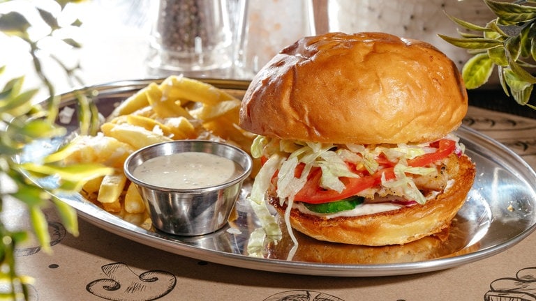 Burger mit Pommes auf einem silbernen Tablett: Eine Studie führt ein gesteigertes Risiko für 32 Erkrankungen auf den Verzehr von hochverarbeiteten Lebensmitteln zurück, darunter Diabetes Typ 2, Adipositas, Herzinfarkt oder Krebs. 