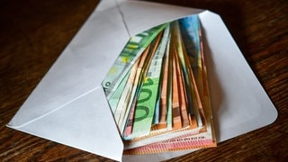 Symbolbild: Mehrere Geldscheine, die in einem Briefumschlag stecken. Nach einer Sitzung der Haushaltskommission hat das Finanzministerium mitgeteilt, wie die Milliarden Euro an Sondervermögen des Bundes verteilt werden sollen. Es soll vor allem in Straßen, Brücken, Schienen, Unikliniken und Landesgebäude investiert werden. 