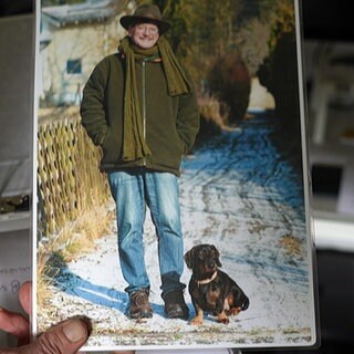 Eine Hand hält ein Bild von Georg und seinem Rauhaardackel Camillo. Gerog lächelt, Camillo steht mit seinen kurzen Beinen im Schnee.