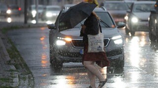 Eine Person in Regenmantel und mit Schirm überquert eine Straße in der Stadt bei Regen. So sah es am Montagabend vielerorts in Rheinland-Pfalz und weiten Teilen von Deutschland aus.