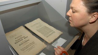 Eine Frau betrachtet den Reichsdeputationshauptschluß aus dem Jahr 1803.