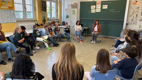 Kinder sitzen im Stuhlkreis in einer Schule. Tina Rastätter und ihre Kolleginnen zeigen Kindern an Schulen, wie sie sich in schwierigen Situationen richtig verhalten.