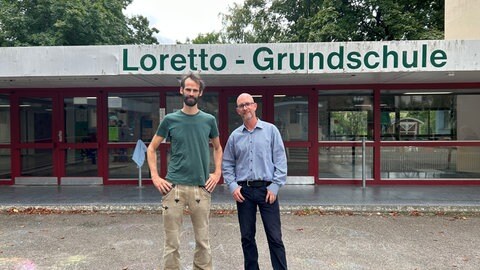 Ein Schulleiter und ein Anwohner stehen vor einer Grundschule in Freiburg.