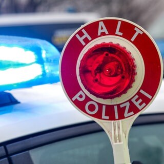 Eine Warnkelle vor einem Streifenwagen (Symbolbild). In Rot am See haben Polizisten einen älteren Autofahrer gestoppt. Seine 88-jährige Beifahrerin ging daraufhin auf die Beamten los.