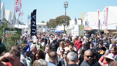 Viele Besucher auf einer Straße beim Mannheimer Maimarkt. Die Besucher laufen an einem sonnigen Maimarkttag die Straße zwischen den Zelten entlang. 