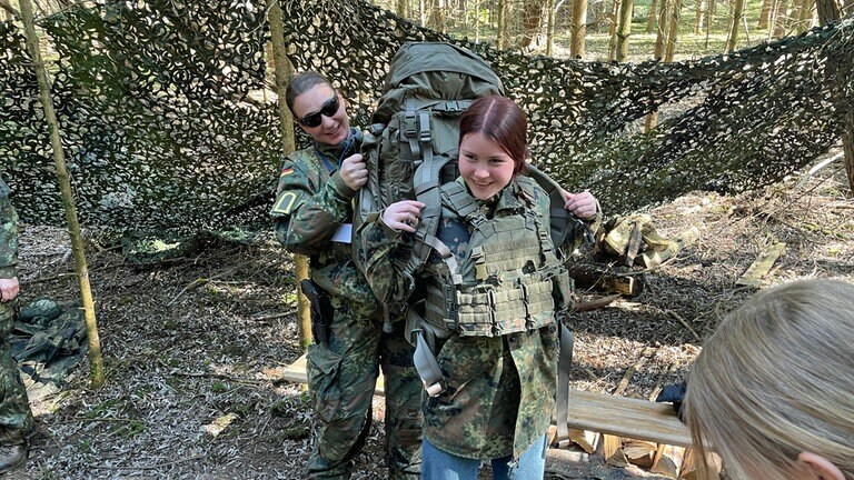 Bis zu 20 Kilogramm Marschgepäck sind schwerer als man denkt. Die Mädchen durften die Rucksäcke probehalber aufsetzen – und bringt sie dabei schon mal ins Wanken.
