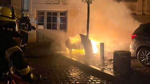 Feuerwehrleute löschen einen brennende Mülltonne in Wiesbaden.