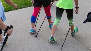 Zwei Personen laufen mit Nordic Walking Stöcken auf einem Weg. Was früher als Training für Biathleten gedacht war, ist heute für viele zum Sport für den Alltag geworden - Nordic Walking. Was ist das genau, und wie effektiv ist dieser Sport?