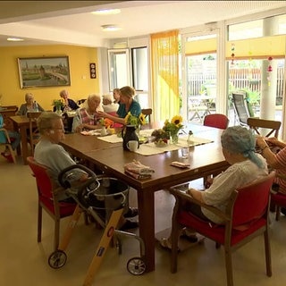 Senior:innen sitzen am Tisch im Pflegeheim