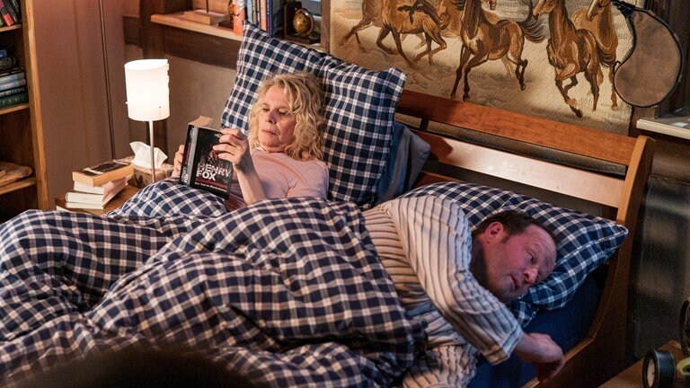 Kati und Bernd liegen im Bett. Sie liest, er versucht zu schlafen.