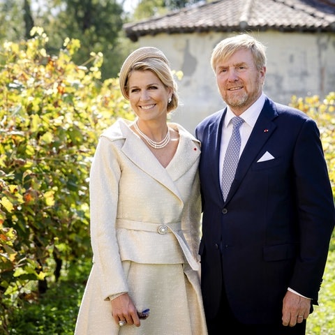 Königin Máxima und König Willem-Alexander stehen zwischen Weinreben in Südfrankreich und tragen schicke Kleider. 