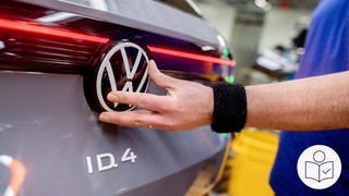Ein VW-Mitarbeiter montiert das Firmenlogo auf der Rückseite eines Elektroautos. Rechts das SWR Logo für Leichte Sprache.