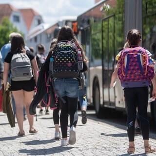 Schülerinnen gehen an einer Bushaltestelle in der Innenstadt zu stehenden Bussen.