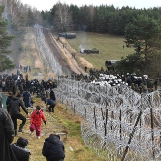 Polnische Polizisten und Soldaten (rechts) bewachen am 8.11.2021 die Grenze in der Nähe eines Migrantenlagers an der weißrussisch-polnischen Grenze in der Region Grodno  Belarus. Hunderte von Migranten aus dem Nahen Osten und Nordafrika versuchten, die Grenze von Weißrussland nach Polen zu überwinden. Aus Sicht der EU benutzt Belarus die Flüchtlinge, um Druck auf die EU auszuüben.