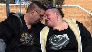 Lukas und Kathi aus Ostfildern sitzen auf einer Bank im Freien und lehnen verliebt die Köpfe aneinander.