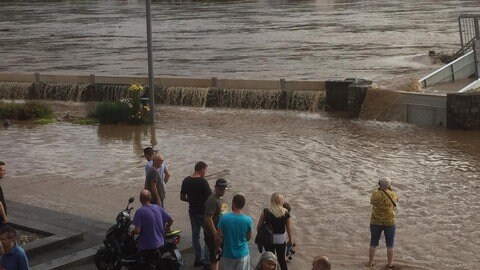 Menschen in Zell an der Mosel stehen vor Wassermassen an einer Hochwassermauer