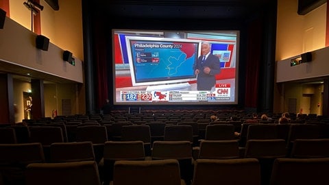 Menschen sitzen im Kinosaal und sehen sich die Übertragung des Senders CNN auf der Leinwand an, um die Wahl in den USA zu verfolgen.
