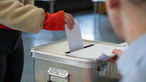 Eine Frau steckt ihren Stimmzettel für die Bundestagswahl in einem Wahllokal in eine Wahlurne. 