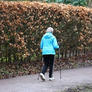 Seniorin geht mit Stöcken spazieren.
