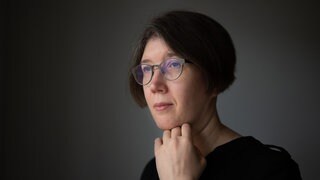 Inna Hartwich hält ihre Hand ans Kinn und schaut seitlich an der Kamera vorbei.