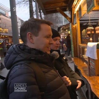 Zwei Lebensmittelkontrolleure stehen am Bratwurststand auf dem Mannheimer Weihnachtsmarkt