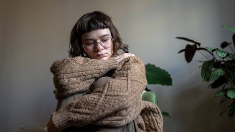 Eine unglückliche Frau sitzt allein zu Hause, umarmt ihre Knie und schaut gleichgültig auf den Boden. Prokrastination kann noch weitere Ursachen haben: Aus weiteren Studien ist bereits bekannt, dass unser Startknopf manchmal auch aus emotionalen Gründen klemmt.