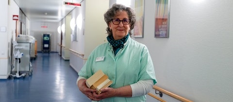 Eine Frau steht in einem Kittel im Flur eines Krankenhauses. Sie ist Grüne Dame im Evangelischen Krankehaus Bad Dürkheim.