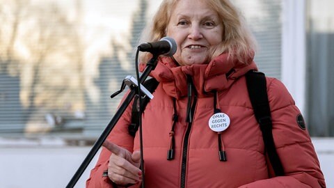 Die Gründerin von „Omas gegen Rechts” Anna Ohnweiler ist bei einer Demonstration und steht auf einer Bühne. Sie steht an einem Mikrofon und schaut in die Kamera.