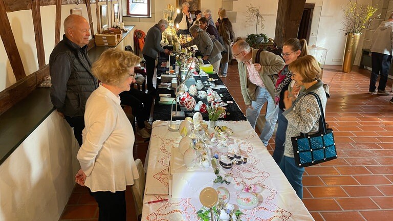 Besucher betrachten filigran bemalte Ostereier auf dem Ostereiermarkt im historischen Rathaus.