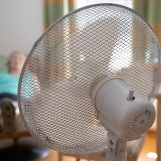 Eine Seniorin sitzt in einem Sessel und wird von einem Ventilator gekühlt. Viele Senioren leiden unter der Hitze.