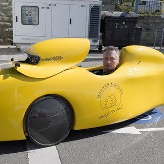 Albrecht Maurer sitzt in seinem knallgelben Velomobil und steht damit auf einer Fahrradstraße. Es ist nur Albrechts Kopf zu sehen, der aus dem Velomobil heraus schaut.