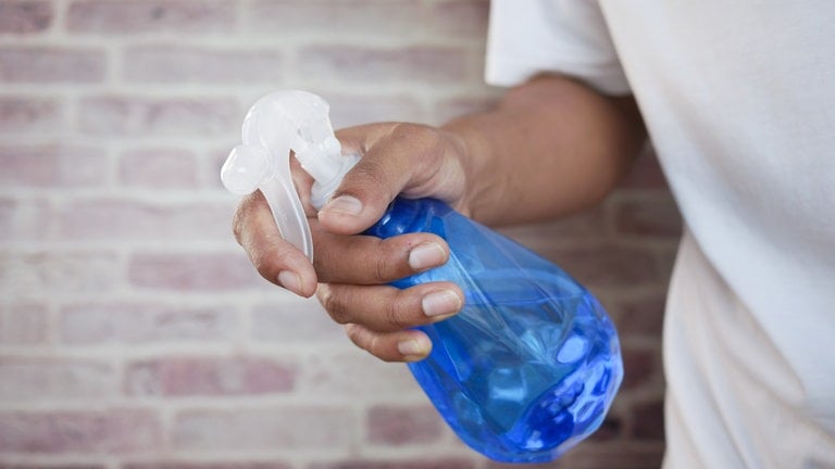Eine Person hält eine blaue Sprühflasche in der rechten Hand