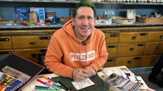 Mann mit grünen Haaren und orangenem Pullover.