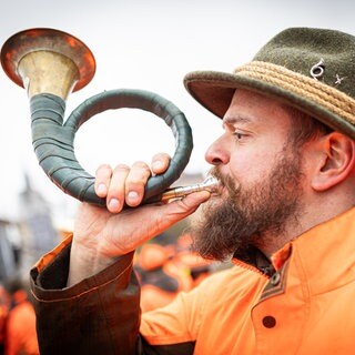 Ein Jäger nimmt an einer Demonstration gegen Jagdbeschränkungen teil und bläst dabei ein Jagdhorn.