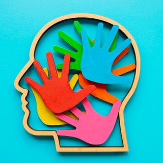 Umriss eines Kopfes mit farbigen Handflächen im Inneren. Abstraktes Symbol für Autismus oder Neurodiversität: Über autistische Menschen gibt es viele Vorurteile und oft wenig Wissen