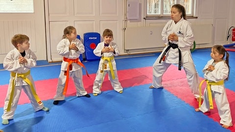 SWR1 Neuanfang: So wurde Mey Alasadi vom Mobbing Opfer zur Karate Meisterin. Mey übt mit Schüler:innen ihrer Karateschule eine Karate-Position. Spielerisch und sportlich lernen die Kinder so Stärke, Selbstbewusstein und Resilienz.