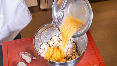 Verquirlte Eier werden aus einer Schale mit Schneebesen über die Brötchen-Milch Masser für die Knödel mit Pfälzer Leberwurstfüllung gegossen.
