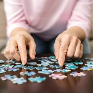 Hände einer älteren Person mit Puzzleteilen an einem Tisch