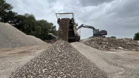 Ein Bagger lädt Steine in einen Pulverisierer. So wird die Gänstorbrücke in Ulm Stück für Stück zerkleinert.
