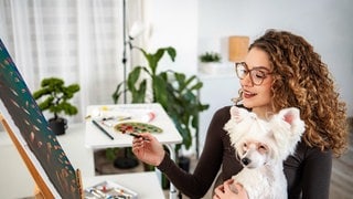 Psychologe bestätigt: Hobbys entspannen und sind gut für Geist und Wohlbefinden | Frau mit Hund vor einer Staffelei