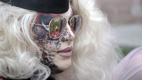 Dragqueen Macy M. Meyers im Profilfoto. Sie trägt einen platinblonde Perücke, aufwändiges Make-up und eine goldgerahmte Sonnenbrille. Sie hat einen Nasenring.