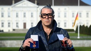 Fotograf Luigi Toscano steht vor dem Schloss Bellevue und hält in der Hand Verdienstmedaille und Verdienstkreuz. 
