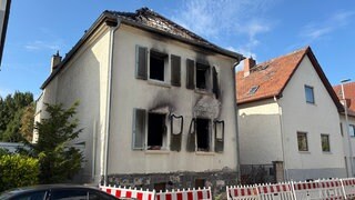 Ein ausgebranntes Haus mit verrußten Fensterhöhlen und zerstörtem Dachstuhl.