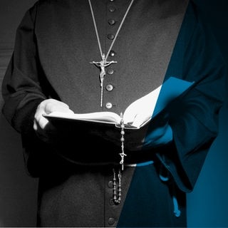Priester in Soutane hält eine Bibel in den Händen