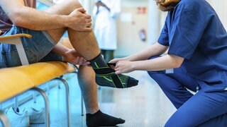 Eine Krankenschwester bandagiert den verletzten Knöchel eines männlichen Patienten in einem Krankenhaus und bietet Unterstützung und Pflege