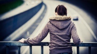 Eine junge Frau steht am Geländer einer Autobahnbrücke.