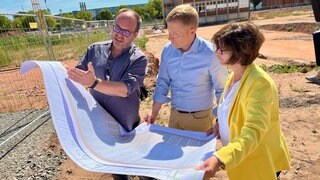 Rolf Crolly, Michael Marschall und Andrea Bergsträßer (von links) vom Westpfalz-Klinikum schauen sich die Pläne für den neuen Gesundheits-Campus am Westpfalz-Klinikum an.  