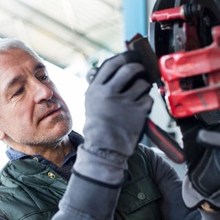 Auto-Mechaniker in Nahaufnahme wechselt Bremsbeläge aus. Woran liegt es, dass oft lange auf Ersatzteile fürs Auto gewartet werden muss?
